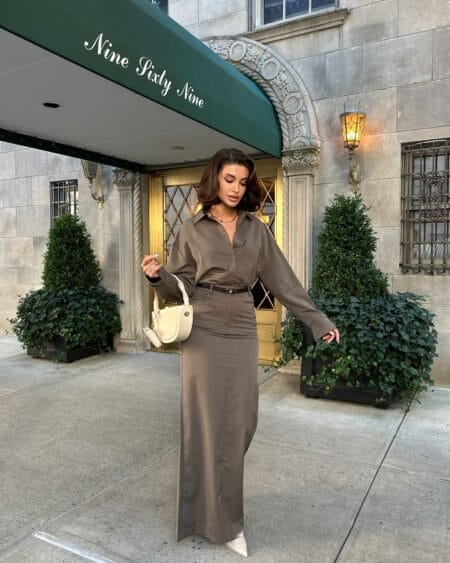 Woman in a taupe shirt and matching floor-length column skirt with a cream half-moon bag
