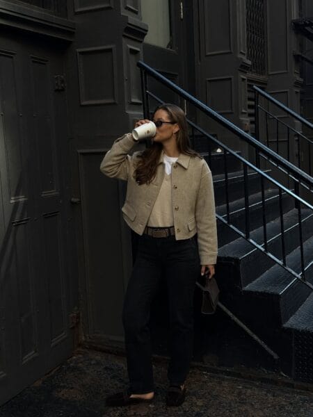 Woman in a cropped oatmeal wool jacket with straight black jeans and dark suede loafers