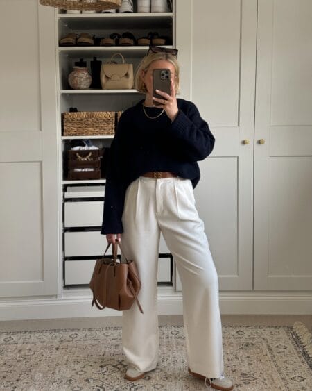 Woman in an oversized navy jumper half-tucked into cream wide-leg trousers with a brown bucket bag