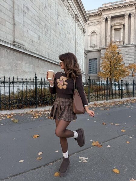 Woman in a brown teddy motif jumper with a plaid pleated mini skirt, sheer tights and platform boots