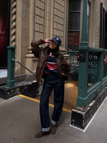 Woman in a vintage brown leather bomber with a navy and burgundy rugby stripe jumper and cuffed jeans