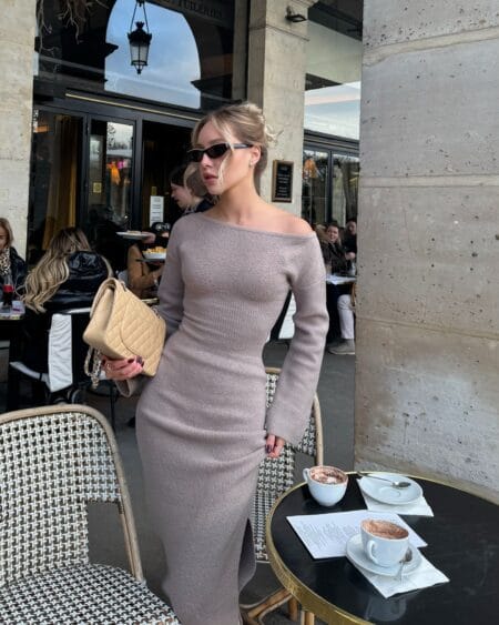 Woman in a mocha off-shoulder ribbed knit maxi dress with a beige quilted flap bag at a cafe