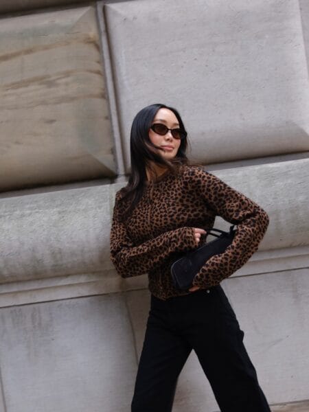 Woman in a brown and black leopard print knit cardigan with straight black jeans and a suede bag