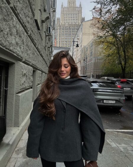 Woman in a charcoal wool jacket with a wide draped scarf collar over a cream turtleneck