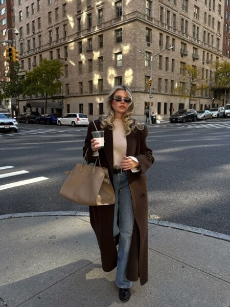 Woman in a floor-length chocolate wool coat with a cream knit and light wash wide-leg jeans