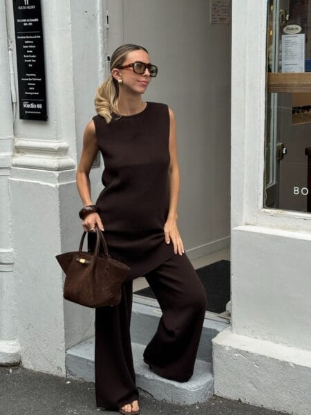 Woman in a sleeveless brown knit tunic over matching espresso wide-leg trousers with a suede tote