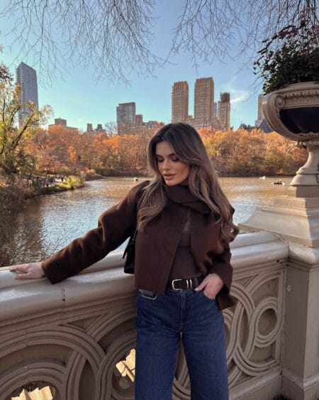 Woman in a chocolate cropped wool jacket with scarf collar and dark indigo wide-leg jeans in Central Park