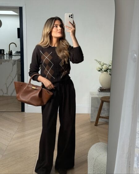 Woman in a brown argyle cardigan and matching wide-leg trousers holding a tan leather tote