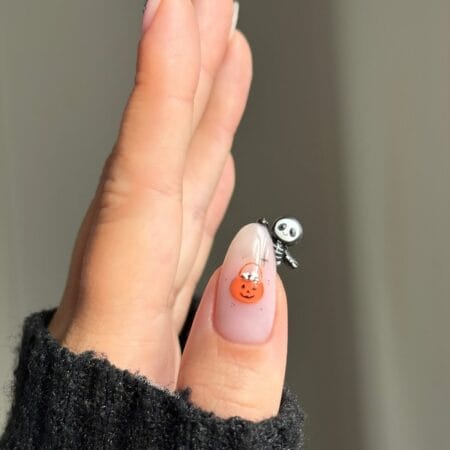 Nude accent nail with 3D skeleton charm and jack-o-lantern