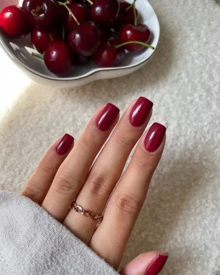 Dark cherry red nails with a glossy almond-shaped finish.
