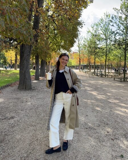 October outfit with beige trench coat, navy jumper and cream straight-leg jeans