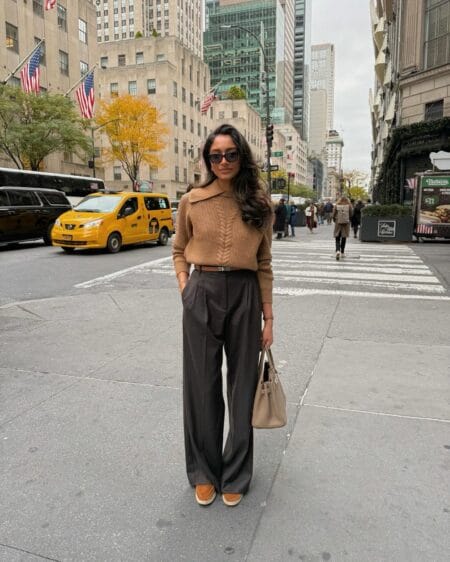 Camel collared cable jumper tucked into chocolate pleated trousers with tan suede loafers in New York