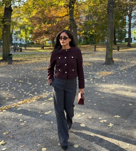Burgundy boucle jacket with gold buttons worn with charcoal wide-leg trousers in an autumn park