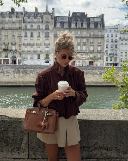 Chocolate silk blouse with gathered shoulders worn with a short cream pleated skirt in Paris