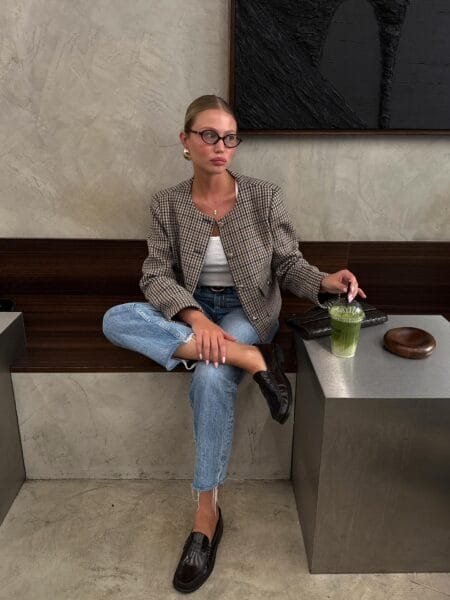 Brown houndstooth collarless jacket over a white vest with light-wash jeans and brown loafers
