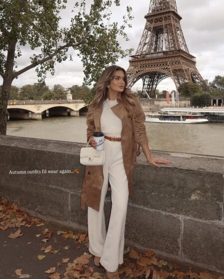 Tan suede trench coat worn open over cream knit and cream wide-leg trousers by the Eiffel Tower