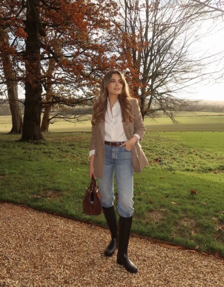 Camel blazer with white shirt, light-wash jeans and tall black riding boots in a countryside setting