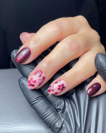Dark cranberry glitter nails paired with translucent jelly accent nails carrying blooming floral artwork