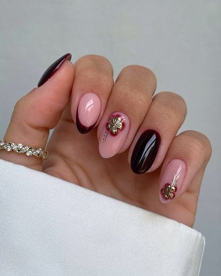 Oxblood French tip nails featuring 3D textured gold flower charms on a blush base