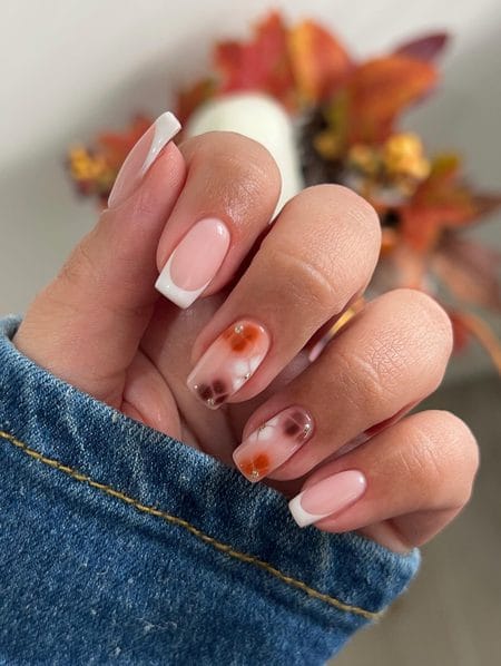 Sharp white French tip nails paired with sheer accent nails carrying burnt orange and brown blooming flowers