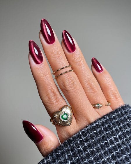 Elongated stiletto nails painted in glowing ruby wine cat-eye magnetic lacquer