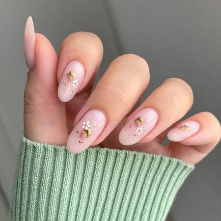 Milky nude almond nails accented with hand-painted gold acorns, white blossoms, and micro dots