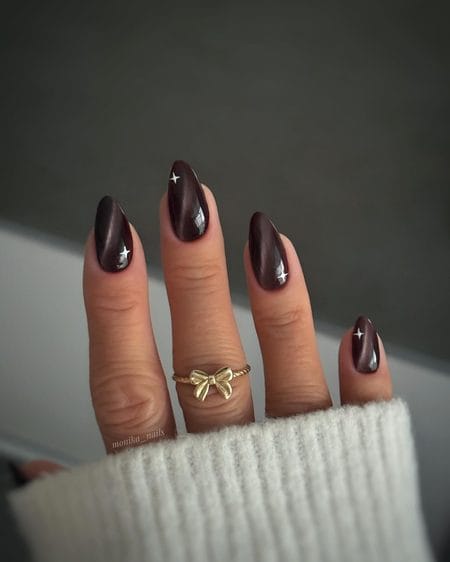 Espresso cat-eye almond nails with bronze shimmer and white starburst accents
