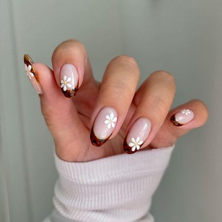 Tortoiseshell French tip nails with delicate white daisy accents on almond nails