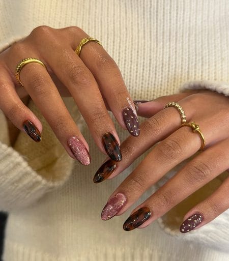 Rose gold cat-eye nails with plum polish, gold studs, and tortoiseshell accents