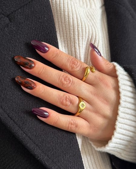 Midnight plum nails with warm caramel tortoiseshell almond accents