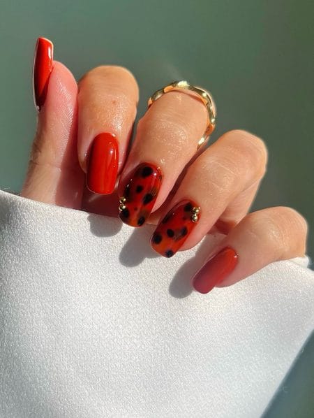 Bright red nails with fiery orange tortoiseshell accents and gold studs